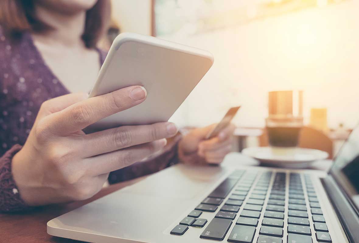 A lady using her phone in front of a laptop