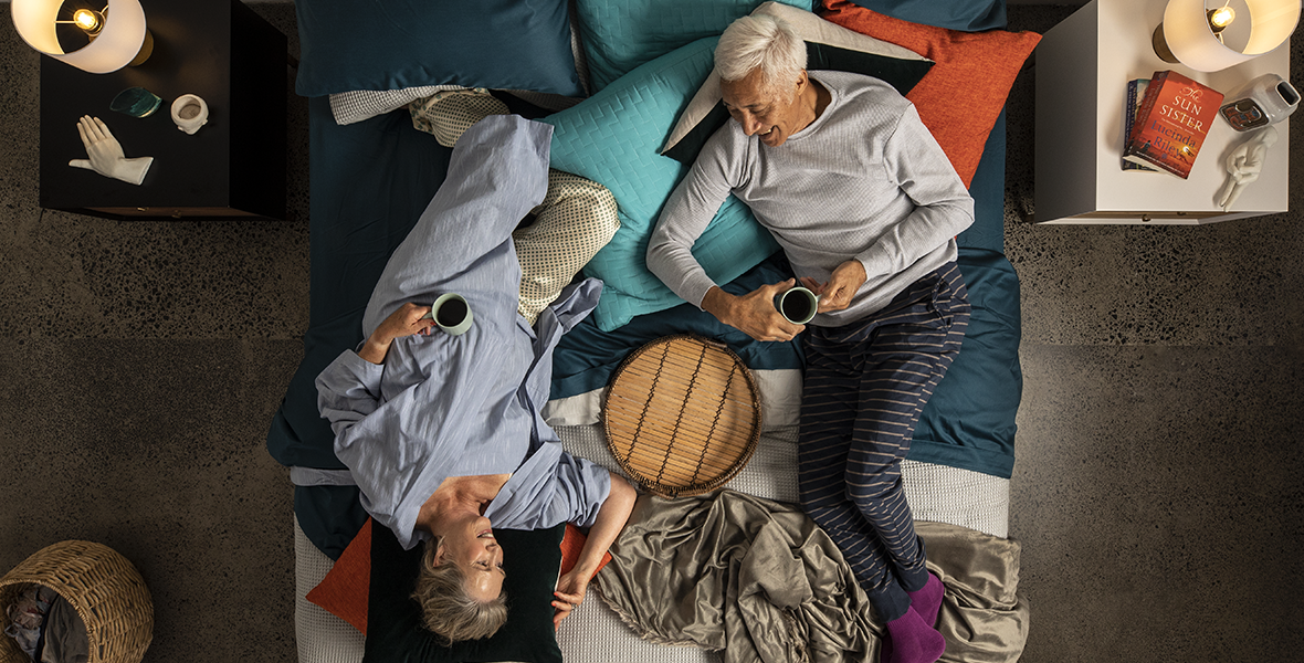 elderly couple lying on a huge bed smiling at each other
